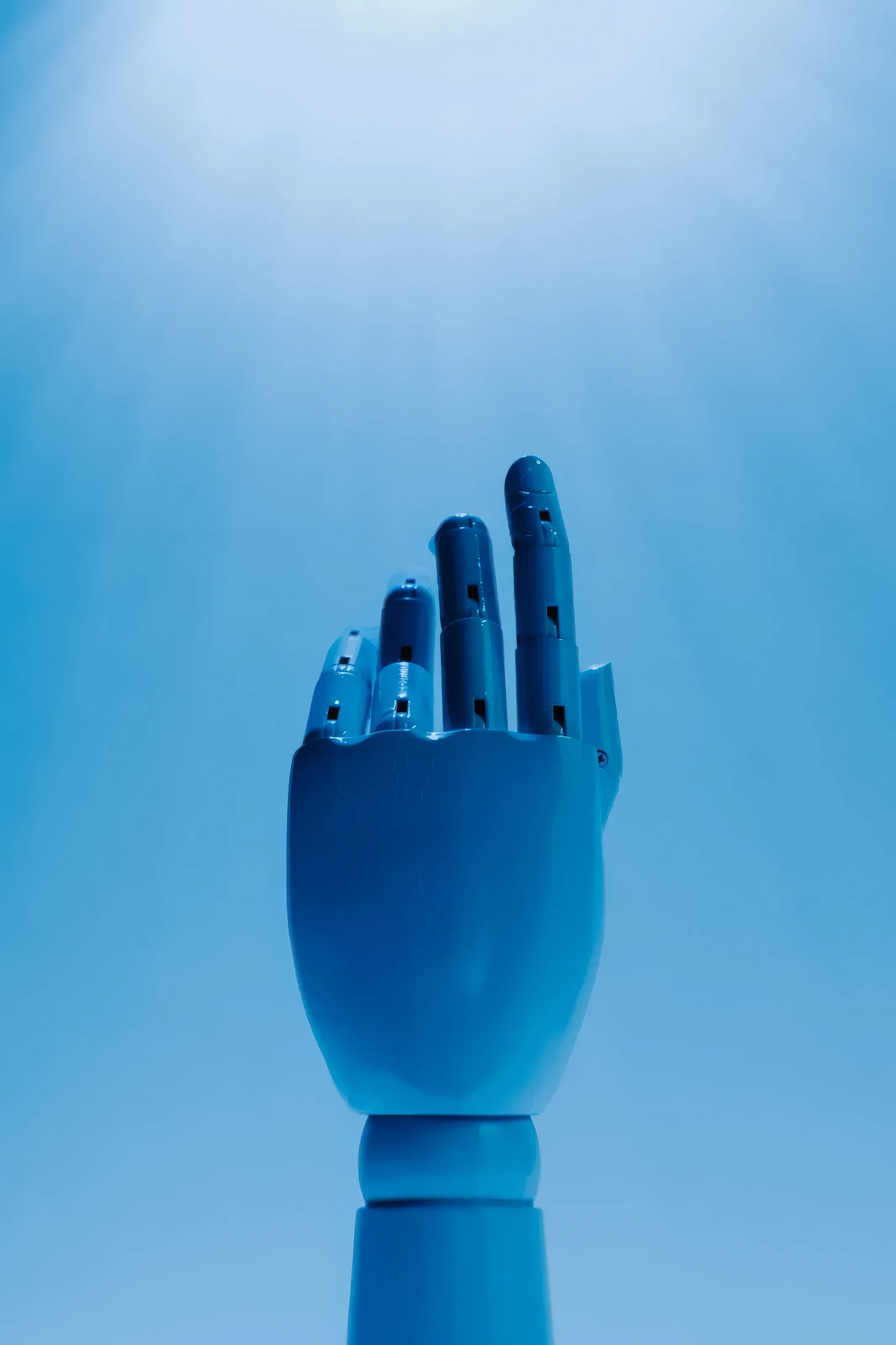 A blue jointed mannequin hand raised against a blue backdrop, lit from above.